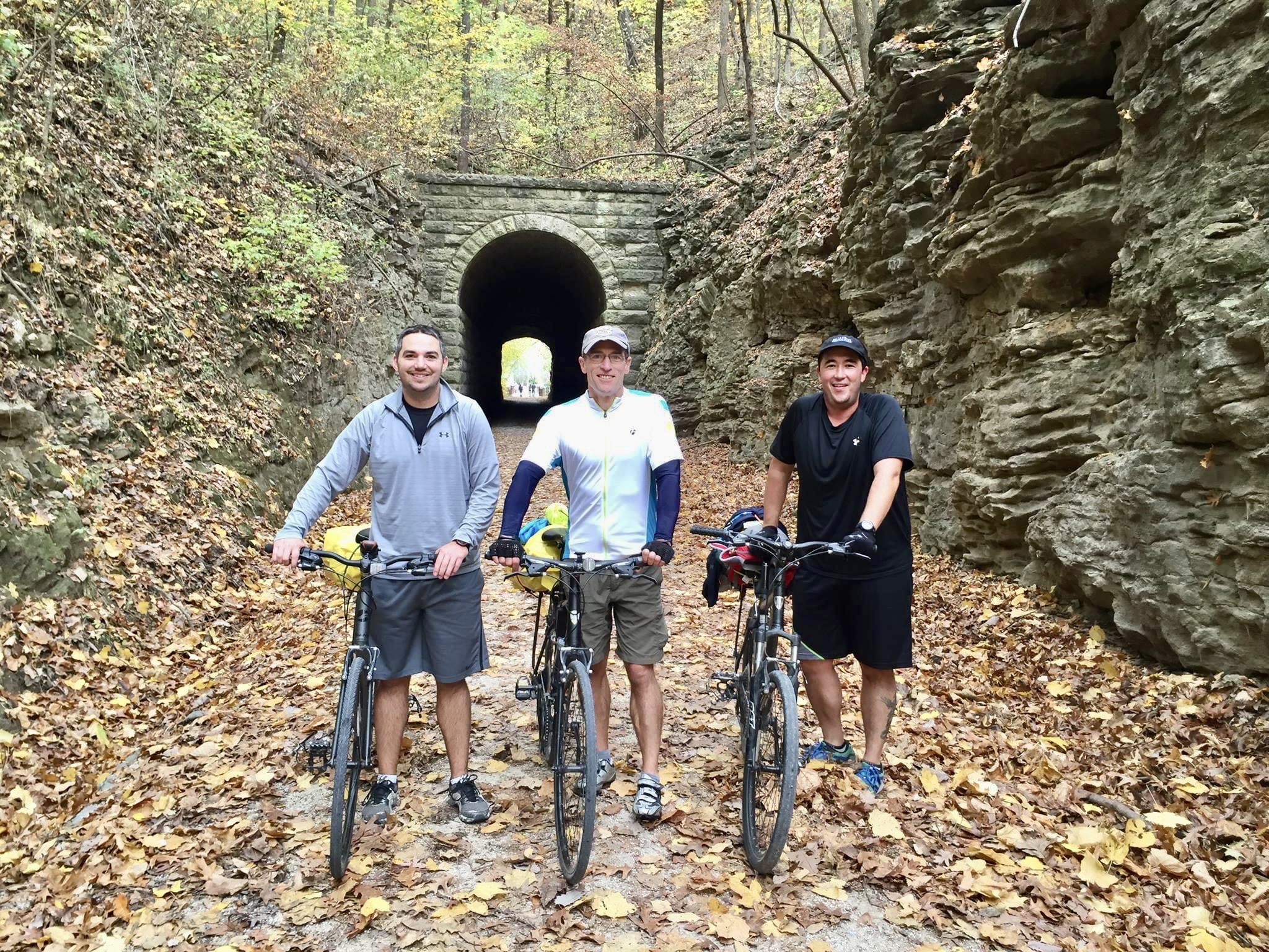 Scenic view of Rocheport Tunnel on the Katy Trail with trees, leaves, and rock and three male cyclists posing with bikes